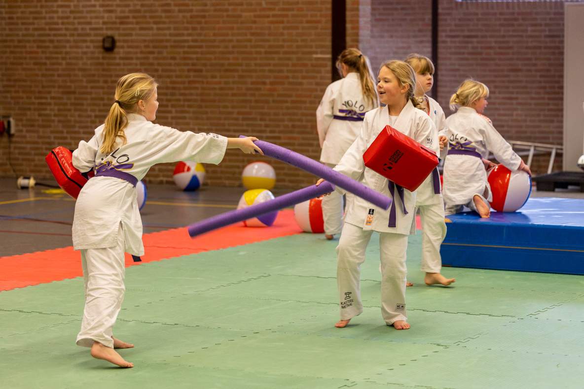 Twee meisjes in judopak stoeien met elkaar